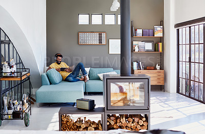 Buy stock photo Shot of a focused young man listening to music through headphones while being seated on a couch at home