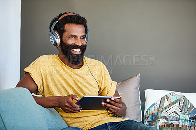 Buy stock photo Shot of a focused young man listening to music through headphones while being seated on a couch at home