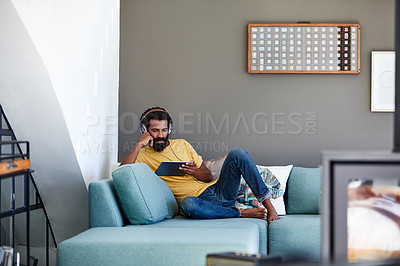 Buy stock photo Shot of a focused young man listening to music through headphones while being seated on a couch at home