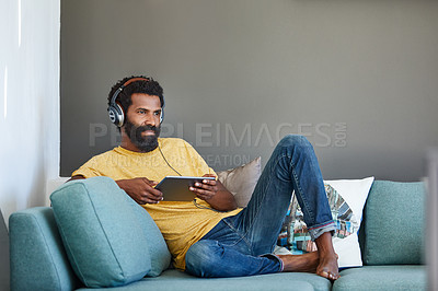 Buy stock photo Shot of a focused young man listening to music through headphones while being seated on a couch at home