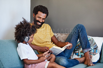 Buy stock photo Shot of a cheerful father and son listening to music and reading a book while relaxing on a couch at home