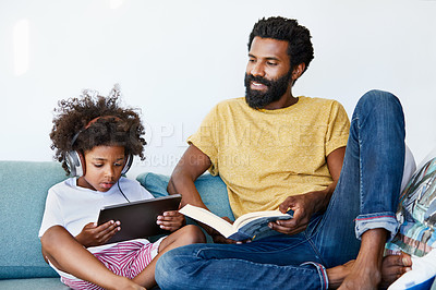 Buy stock photo Shot of a cheerful father and son listening to music and reading a book while relaxing on a couch at home