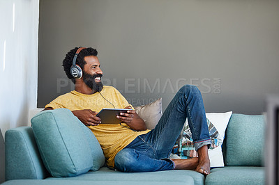 Buy stock photo Shot of a focused young man listening to music through headphones while being seated on a couch at home
