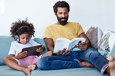 Buy stock photo Shot of a cheerful father and son listening to music and reading a book while relaxing on a couch at home