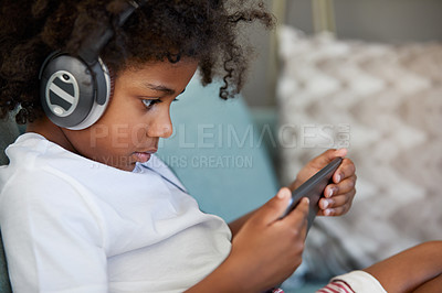 Buy stock photo Shot of a focused little boy browsing on a digital tablet and wearing headphones while relaxing on the couch at home