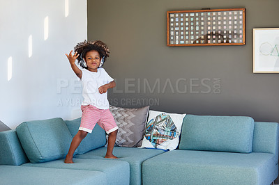 Buy stock photo Portrait of a cheerful young little boy dancing on a couch while listening to music at home during the day