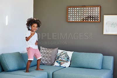 Buy stock photo Portrait of a cheerful young little boy dancing on a couch while listening to music at home during the day