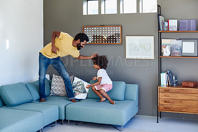 Buy stock photo Shot of a cheerful young father and his son dancing on a couch while listening to music at home during the day