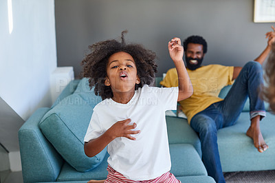 Buy stock photo Shot of a cheerful young father and his son dancing on a couch while listening to music at home during the day