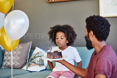 Buy stock photo Shot of a cheerful little boy blowing out candles on a cake that he received from his dad inside at home during the day