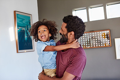 Buy stock photo Shot of a cheerful young man holding his son in his arms while standing in the living room at home during the day