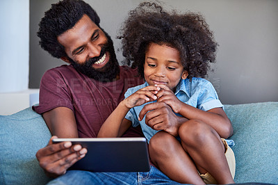 Buy stock photo Shot of a cheerful young father and son browsing on a digital tablet while relaxing on a couch at home during the day