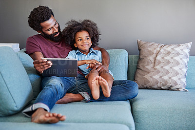 Buy stock photo Shot of a cheerful young father and son browsing on a digital tablet while relaxing on a couch at home during the day