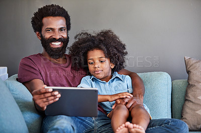 Buy stock photo Portrait of a cheerful young father and son browsing on a digital tablet while relaxing on a couch at home during the day