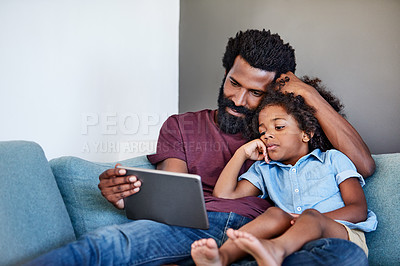 Buy stock photo Shot of a cheerful young father and son browsing on a digital tablet while relaxing on a couch at home during the day