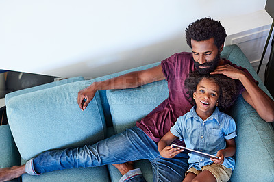 Buy stock photo High angle shot of a cheerful young father and son browsing on a digital tablet while relaxing on a couch at home during the day