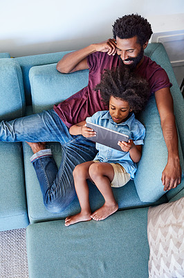 Buy stock photo High angle shot of a cheerful young father and son browsing on a digital tablet while relaxing on a couch at home during the day
