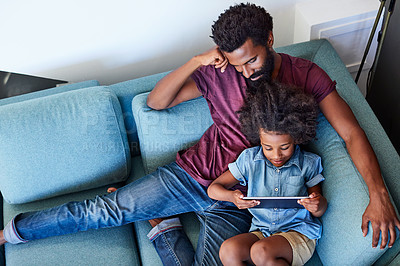 Buy stock photo High angle shot of a carefree young father and son browsing on a digital tablet while relaxing on a couch at home during the day