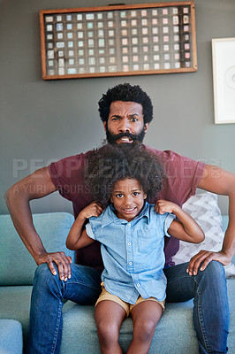 Buy stock photo Portrait of a cheerful father and son flexing their muscles while being seated on a couch at home during the day