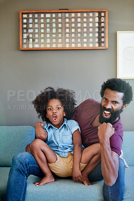 Buy stock photo Portrait of a cheerful father and son striking a pose while being seated on the couch at home during the day