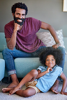Buy stock photo Portrait of a cheerful father and son striking a pose while being seated on the couch at home during the day