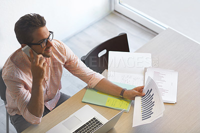 Buy stock photo High angle shot of a businessman talking on his phone while working on some paperwork