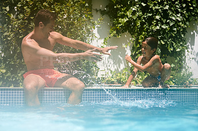 Buy stock photo Shot of a father and son splashing each other at the swimming pool