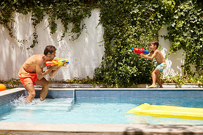 Buy stock photo Shot of a father and his son playing with water guns at the swimming pool