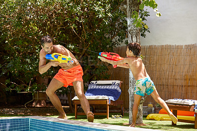 Buy stock photo Shot of a father and his son playing with water guns at the swimming pool