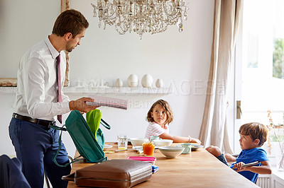 Buy stock photo Cropped shot of a young siblings having breakfast while their father gets their backpacks ready for school