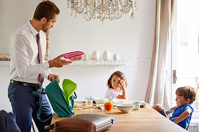 Buy stock photo Cropped shot of a young siblings having breakfast while their father gets their backpacks ready for school
