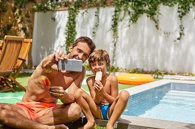 Buy stock photo Shot of a young man and his adorable son taking selfies by the swimming pool