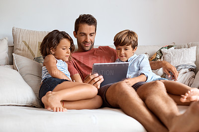 Buy stock photo Shot of a little girl and boy using a digital tablet while sitting with their father