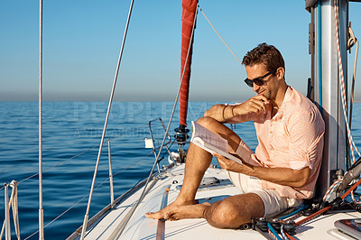 Buy stock photo Shot of a handsome young man reading a book on a relaxing boat cruise