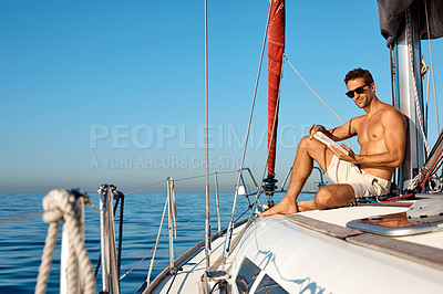 Buy stock photo Shot of a handsome young man reading a book on a relaxing boat cruise