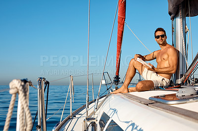 Buy stock photo Shot of a handsome young man reading a book on a relaxing boat cruise