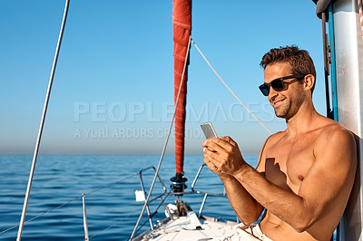 Buy stock photo Shot of a handsome young man using a mobile phone on a relaxing boat cruise