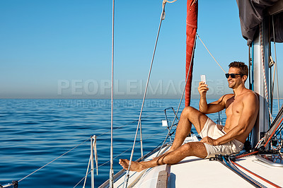 Buy stock photo Shot of a handsome young man using a mobile phone on a relaxing boat cruise