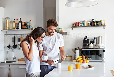 Buy stock photo Shot of a young couple using a digital tablet together during their morning routine at home