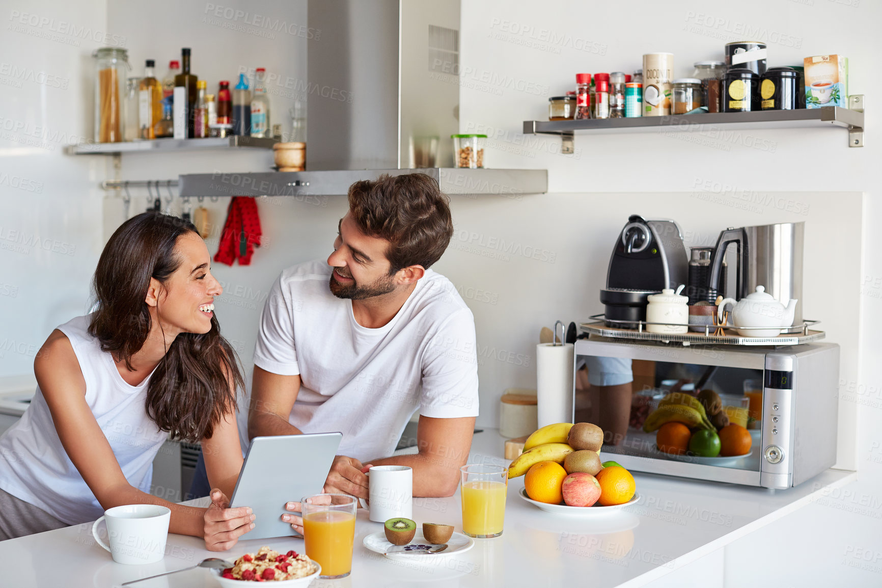 Buy stock photo Breakfast, laughing and tablet with couple in kitchen of home together for start of morning routine. App, food and funny with people at counter in apartment for health, nutrition or wellness info