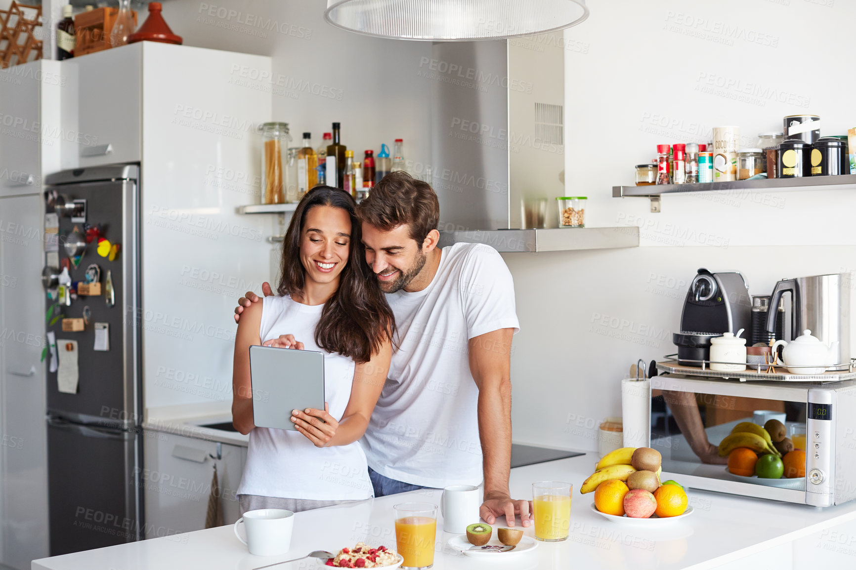 Buy stock photo Breakfast, hug and tablet with happy couple in kitchen of home together for start of morning routine. App, food and reading with people embracing in apartment for health, nutrition or wellness