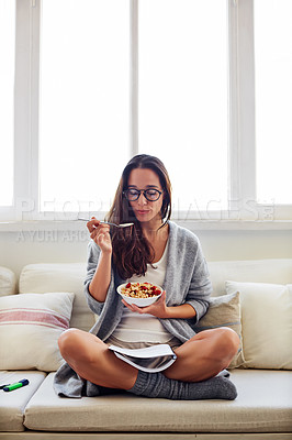 Buy stock photo Shot of a beautiful young woman going over some work while having breakfast in the morning at home
