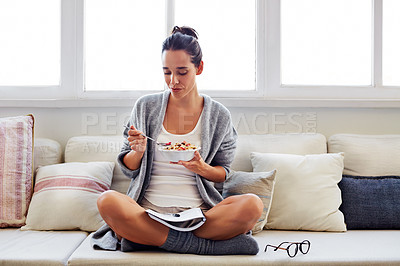 Buy stock photo Shot of a beautiful young woman going over some work while having breakfast in the morning at home