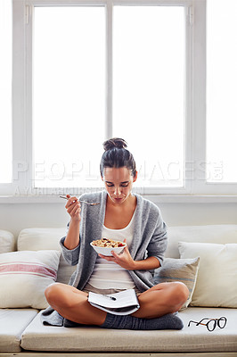 Buy stock photo Shot of a beautiful young woman going over some work while having breakfast in the morning at home