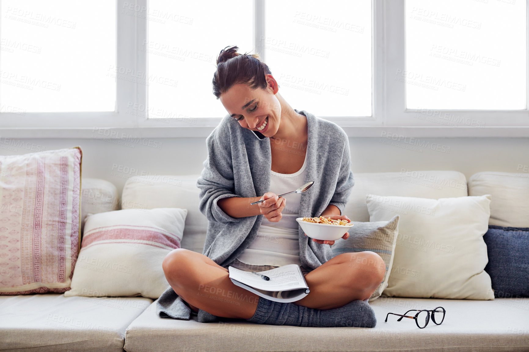 Buy stock photo Shot of a beautiful young woman talking on a mobile phone and working while having breakfast at home