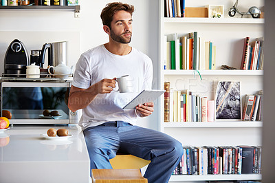 Buy stock photo Shot of a handsome young man using a digital tablet and having coffee in the morning at home