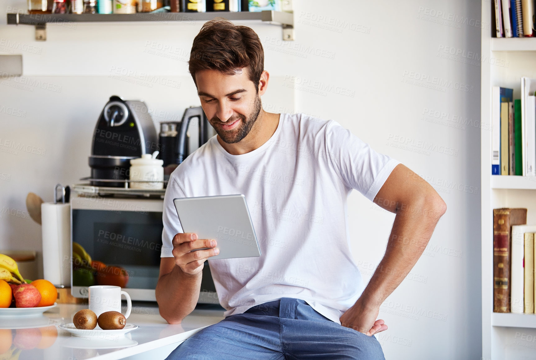 Buy stock photo Shot of a handsome young man using a digital tablet in the morning at home