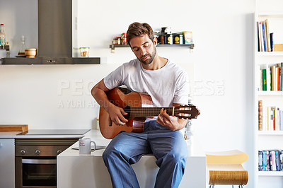 Buy stock photo Shot of a handsome young man playing the guitar in the morning at home