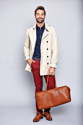 Buy stock photo Studio portrait of a handsome young man carrying a suitcase against a grey background