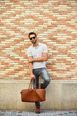 Buy stock photo Shot of a fashionable young man leaning against a brick wall outside